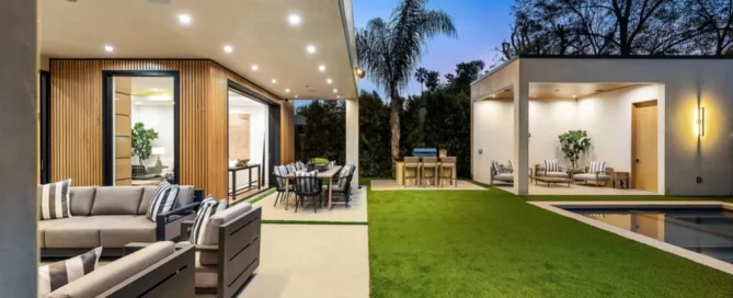 Modern outdoor patio area with comfortable seating, dining table, and a lush green lawn, set against a twilight sky.