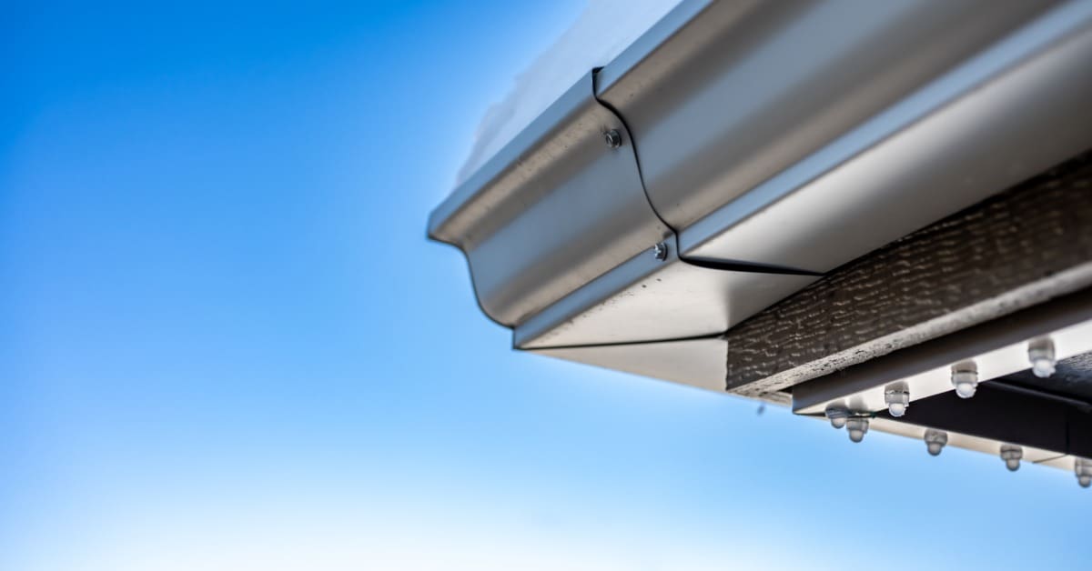A close-up of the a gutter attached to the roof's corner. Permanent lights are installed on the underside of the roof.