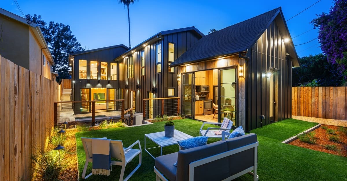 The backyard of a modern home features downlights mounted on the structure and lights embedded in the landscaping.