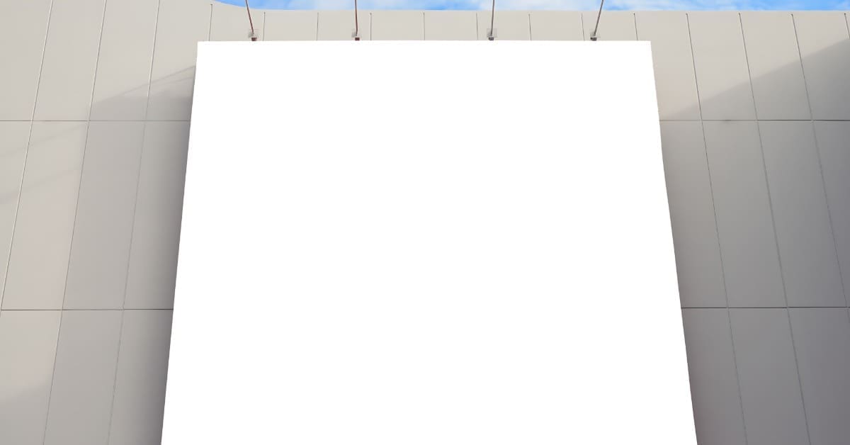 A white, blank billboard is attached to a gray building. Four metal downlights are evenly positioned above the sign.